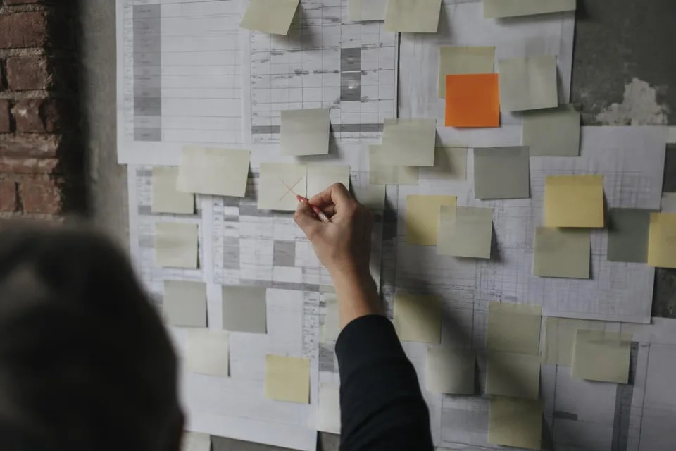 Projektwand voller Haftnotizen, eine Hand streicht ein Projekt durch