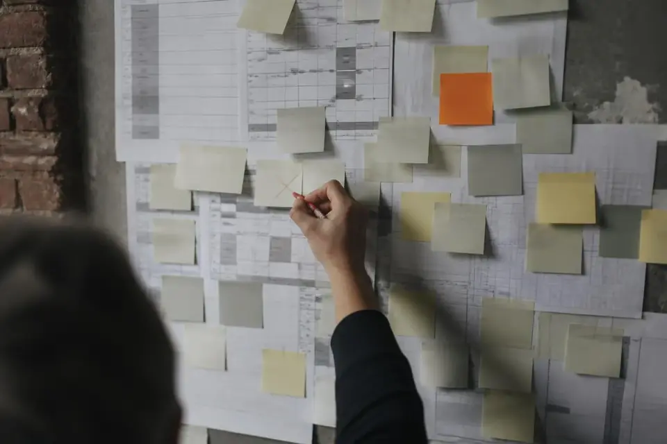 Projektwand voller Haftnotizen, eine Hand streicht ein Projekt durch